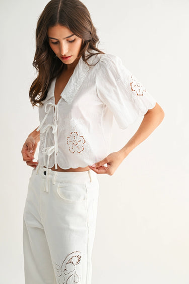 Woman wearing a white embroidered blouse and pants on a plain background