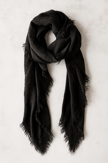 Black lightweight scarf with fringe edges folded on neutral linen background.