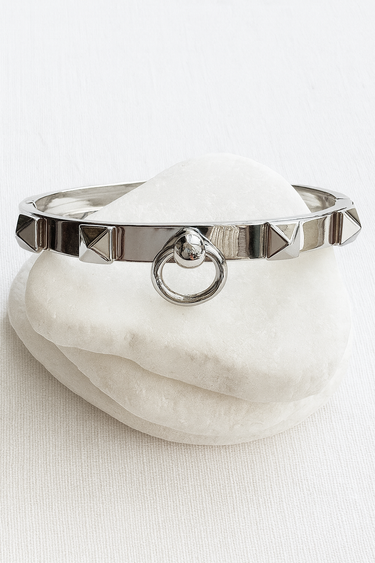 Alaia Bangle Bracelet — silver bangle bracelet with pyramid studs and ring detail on white linen background, polished and bold jewelry by Matte.