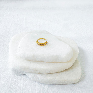 Gold ear cuff on a stack of white stones with a white background