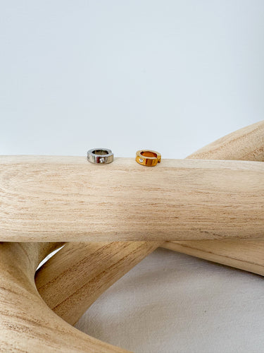 Two ear cuffs, one silver and one gold, displayed on a wooden surface.