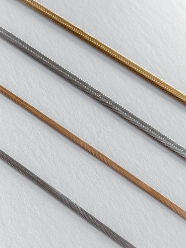 A collection of gold-plated snake chain necklaces laid out parallel to each other on a light surface.