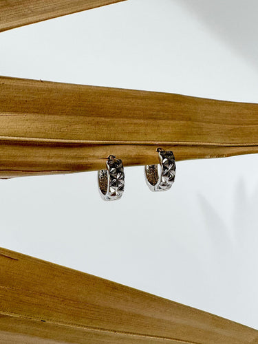A pair of Anais gold-plated huggie earrings displayed on a wooden surface.