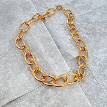 A gold-filled chunky necklace displayed on a wooden stand by Matte