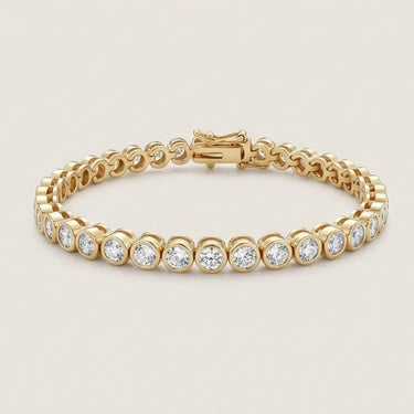 Gold bezel tennis bracelet with round clear stones, polished silver finish, secure clasp closure, and minimalist luxury jewelry styling on a warm light gray background.