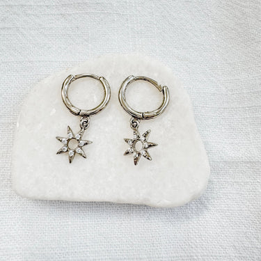 A pair of gold-plated huggie earrings with star charms attached, displayed on a white surface.