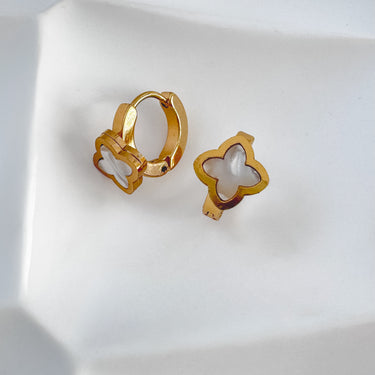 A pair of Arwen gold-colored hoop earrings with white mother-of-pearl accents shaped like clovers, displayed on a white surface.