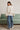 Woman wearing relaxed neutral sweatshirt with dropped shoulders and ribbed cuffs, styled with blue jeans and sneakers, back view.