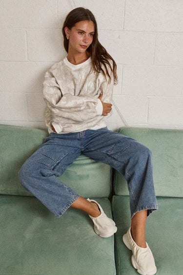 Woman wearing relaxed neutral sweatshirt with dropped shoulders and ribbed cuffs, styled with blue jeans and sneakers.