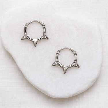 Auri Huggie Earrings — silver spike-detail huggies on white stone background, bold, polished, and lightweight jewelry by Matte.