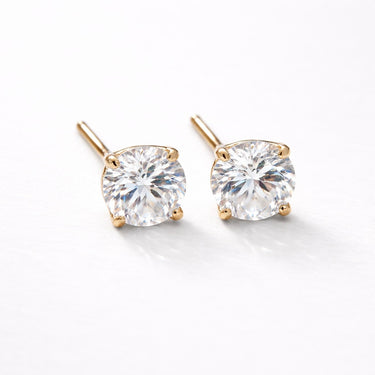 Biela Stud Earrings gold version close-up showing round-cut clear zirconia stones set in gold prong setting on light neutral background with soft shadow