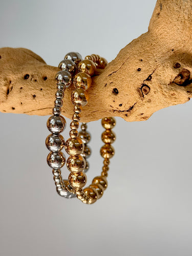 Stack of gold and silver Blasco Bracelets displayed on natural wood branch