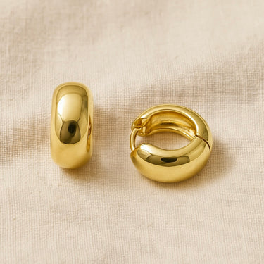 Gold domed huggie earrings on beige linen backdrop — Cairo Huggie Earrings by Matte.