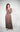 Model wearing Caracol Dress in mocha brown, featuring long sleeves, V-neckline, and ruffled hem.