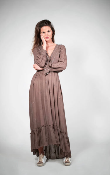 Model wearing Caracol Dress in mocha brown, featuring long sleeves, V-neckline, and ruffled hem.