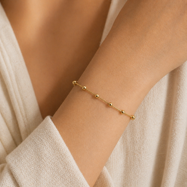 Ceketi Bracelet delicate gold beaded bracelet worn on wrist with cream sleeve, showing minimal chain design and polished bead accents.