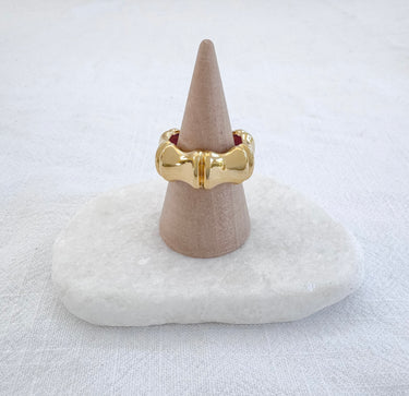 A gold-colored ring displayed on a beige mount, set against a white background.