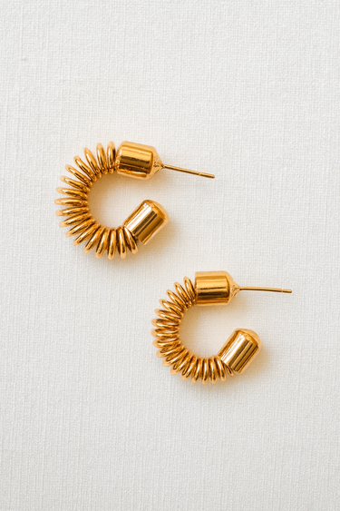 Gold coiled hoop earrings with sculptural spiral design displayed on light fabric background, Cicely Hoop Earrings by Matte.