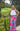 Woman in a white top and colorful pants standing outdoors with greenery around