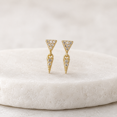 Gold triangle-shaped earrings with embedded stones on a white cushion