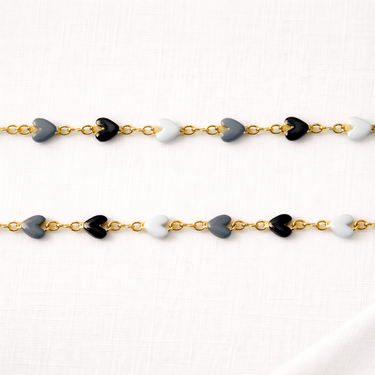 Eloide Necklace laid flat showing black, gray, and white glossy heart charms on gold-tone chain