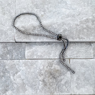 A silver-colored, adjustable rhinestone bracelet laid out on a grey surface.