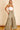 A female model wearing a white tube top and green wide leg pants with a high waist and tiered design.