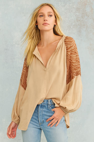 Woman wearing Evalina Blouse in beige silk with embroidered animal-texture sleeves, styled with denim jeans.