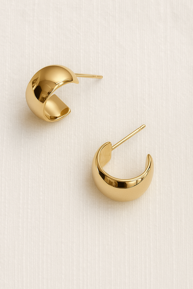 Evelina Hoop Earrings featuring polished gold-plated mini hoop earrings with a sculptural puffed C-shaped silhouette, smooth mirror finish, lightweight hollow design, secure post-back closure, and elegant everyday style, displayed on a soft neutral background.
