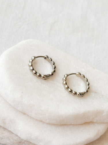 Pair of silver Francesca mini huggies earrings on a white stone surface