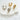 Four Gala Huggie Earrings in gold and silver finishes resting on a white stone against a neutral fabric background.