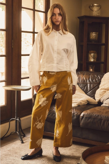 Full-length front view of Galicia Pant featuring mustard floral fabric, relaxed wide-leg fit, and cropped hem styled with black ballet flats.