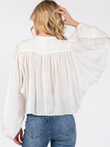 Model wearing the Giselle Blouse in white — semi-sheer, lightweight button-down with voluminous sleeves, styled with denim jeans against a neutral background, back view.