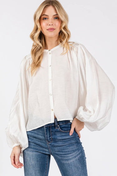 Model wearing the Giselle Blouse in white — semi-sheer, lightweight button-down with voluminous sleeves, styled with denim jeans against a neutral background, front close up.