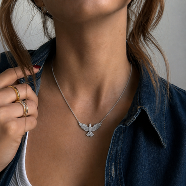Grim Necklace silver-tone phoenix pendant necklace worn on model with dark shirt, showing bold pendant silhouette at neckline.