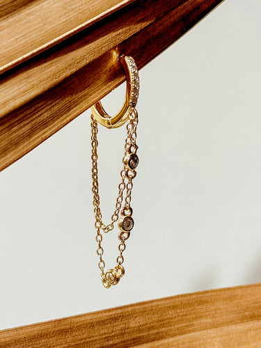 A gold-filled hoop earrings with a chain and small pave crystals, displayed on a wooden surface.
