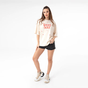 Happy Hour T-Shirt full outfit view showing oversized cream t-shirt, red graphic print on chest, loose short sleeve silhouette, styled with neutral sneakers, photographed on white studio background.