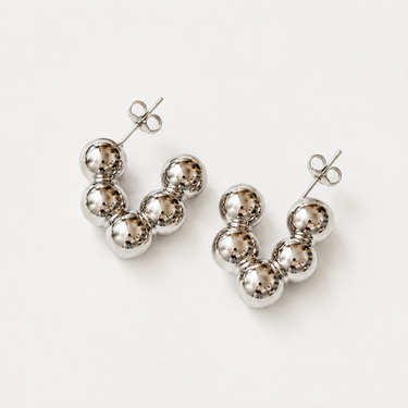 Hasselt Hoop Earrings featuring polished silver-plated hoop earrings with graduated sphere bead clusters, a sculptural rounded silhouette, mirror finish, secure post-back closure, lightweight design, and bold contemporary style, displayed on a soft white background.