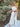 Woman in a white dress with a brown Scarlet knot belt standing in a garden.