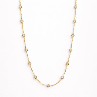 Iki Necklace gold zirconia version flat lay showing fine chain with small bezel-set clear stones on light neutral background with soft shadow.