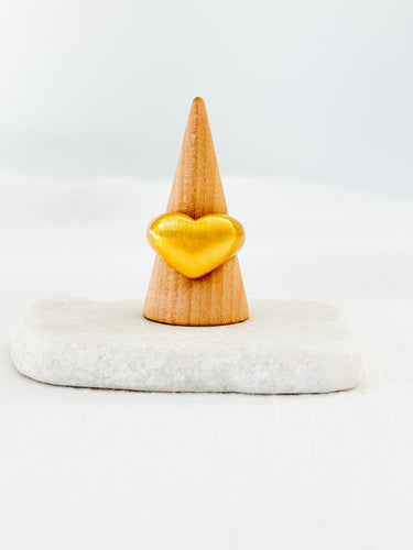 A gold-filled heart-shaped ring displayed on a wooden stand against a white background.