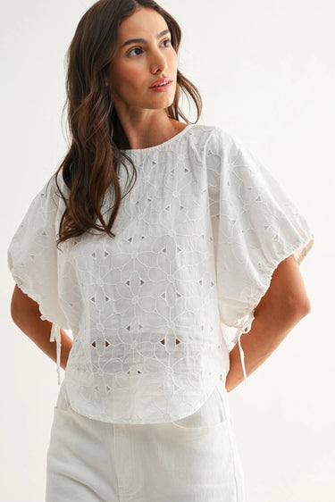 Woman wearing a white blouse with intricate patterns on a plain background