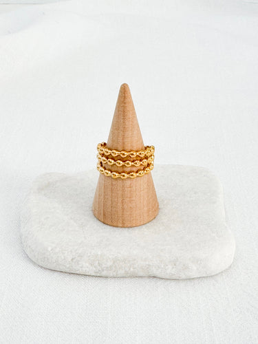 A gold-plated beaded ring displayed on a wooden stand with a white cushion