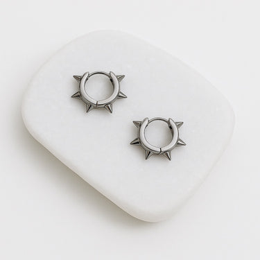 A pair of Juliette stainless steel huggie earrings with a spike design, displayed on a white surface.