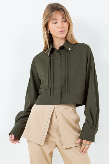 Woman wearing the Kairo Blouse in olive green, refined cropped silhouette with pintuck detailing and gold collar charms, photographed on a clean white background.