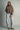 Model wearing the Karls Jacket in taupe with diamond quilting and a padded stand collar, styled with printed light-wash jeans and tan clogs.