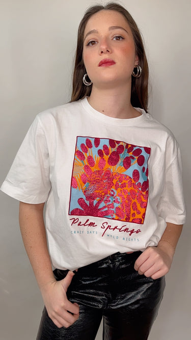 Model wearing the Katerina Tee — white cotton t-shirt with colorful Palm Springs graphic print, relaxed fit, short sleeves, modern casual style.