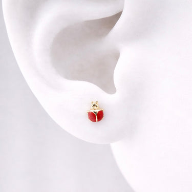 Ladybug Stud Earrings worn on ear featuring glossy red enamel ladybug design with black detailing and gold accents, shown on a model ear against a soft neutral background, small dainty everyday stud earrings.