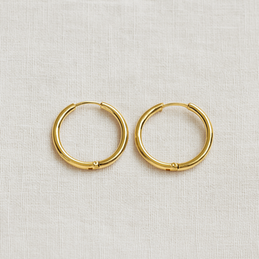 Linea Huggie Earrings, slim gold huggie hoop earrings with smooth polished finish, photographed on white linen background with soft editorial lighting.