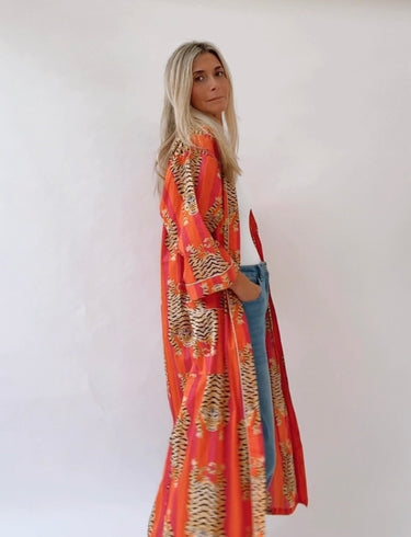 Woman wearing Mosaic Tiger Duster Kimono, long orange cotton kimono with tiger print and flowing sleeves.